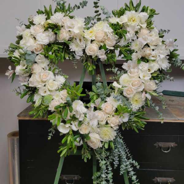 Heart-shaped white floral wreath with roses and lilies on a stand