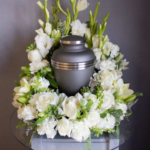 Cremation urn encircled by white roses, lilies, and carnations in a wreath-style arrangement
