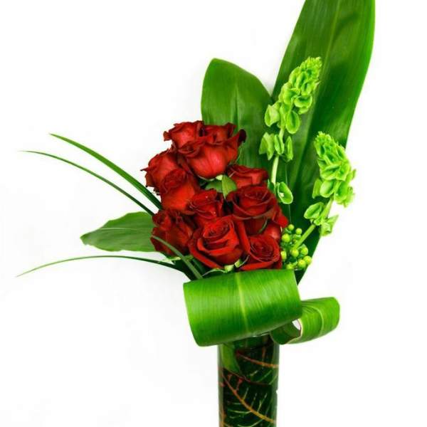 Red roses arranged with green leaves in a tall glass vase