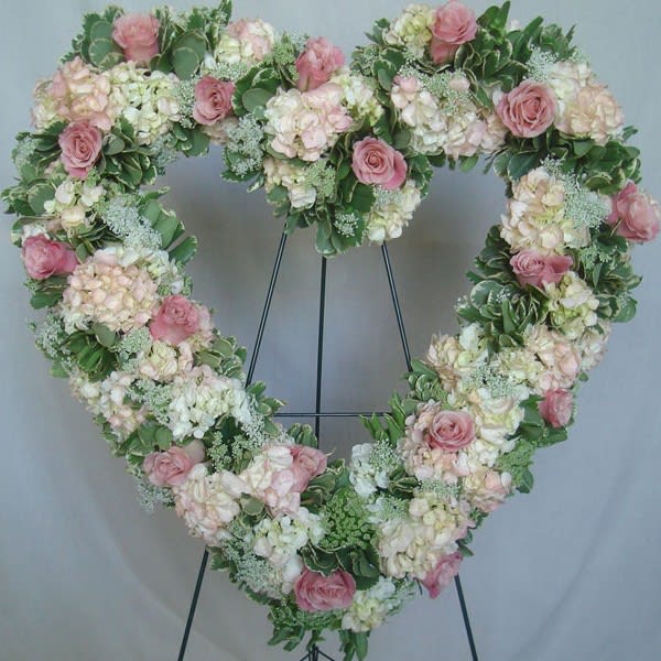 Heart-shaped floral wreath with pink roses and pale hydrangeas on a stand