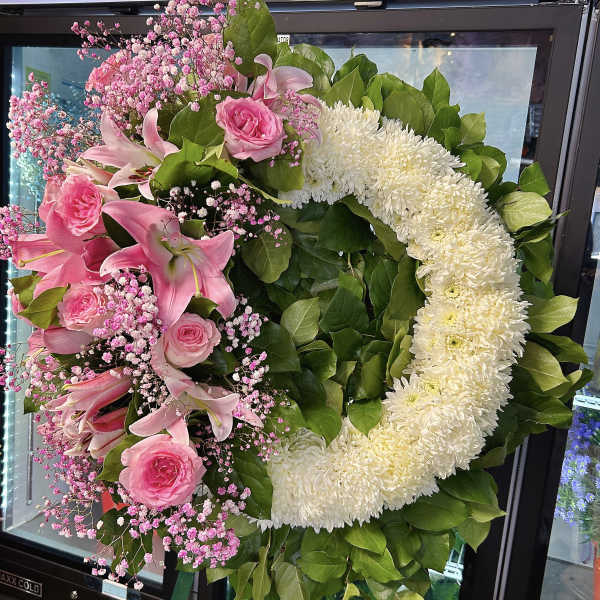 Pink lilies and roses arranged in a heart-shaped wreath with white flowers.