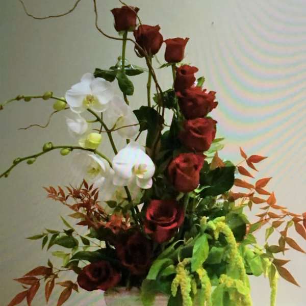 Tall arrangement of red roses and white orchids in a white vase