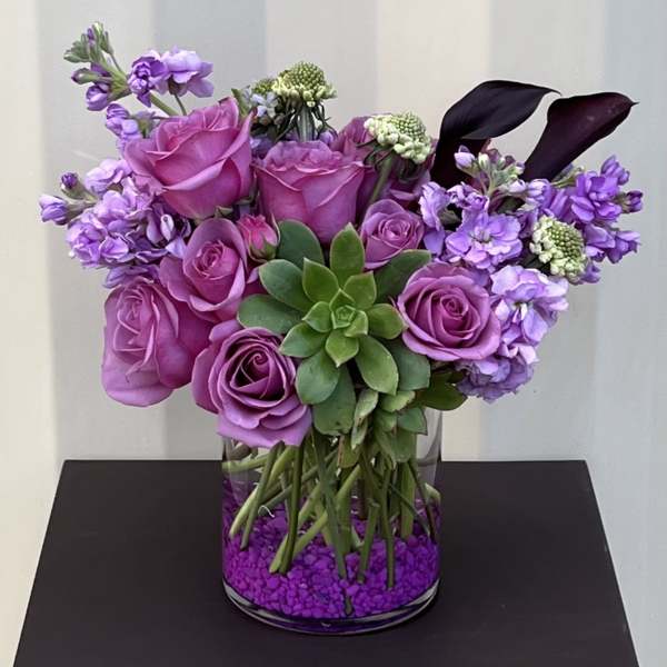 Purple roses and lavender flowers arranged in a glass vase with a succulent center.