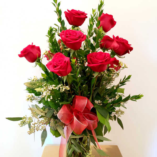 Red roses arranged in a clear glass vase with a pink ribbon