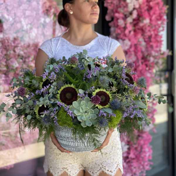 Woman holding a large mixed floral arrangement in a patterned bowl
