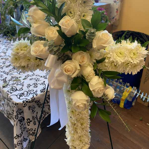 White roses and chrysanthemums arranged on a standing cross with a white ribbon.