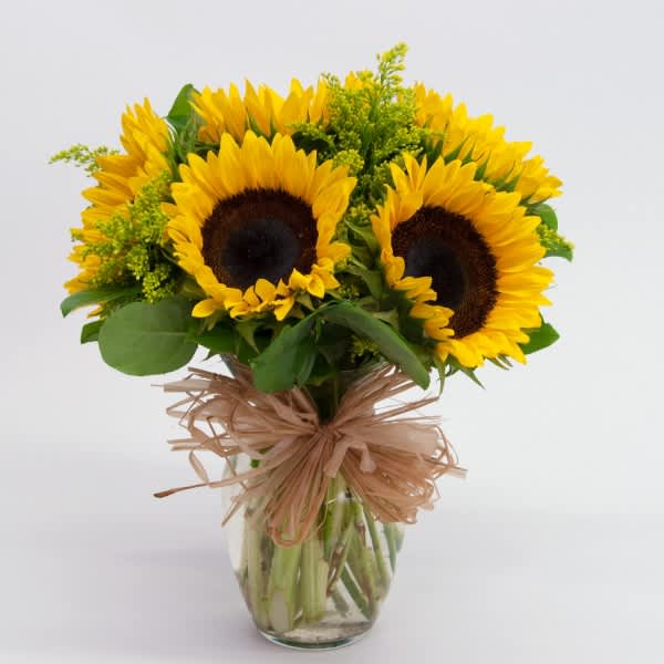 Bouquet of sunflowers in a clear glass vase with a raffia bow