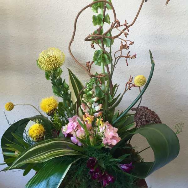 Tall floral arrangement with yellow and pink blooms in a container