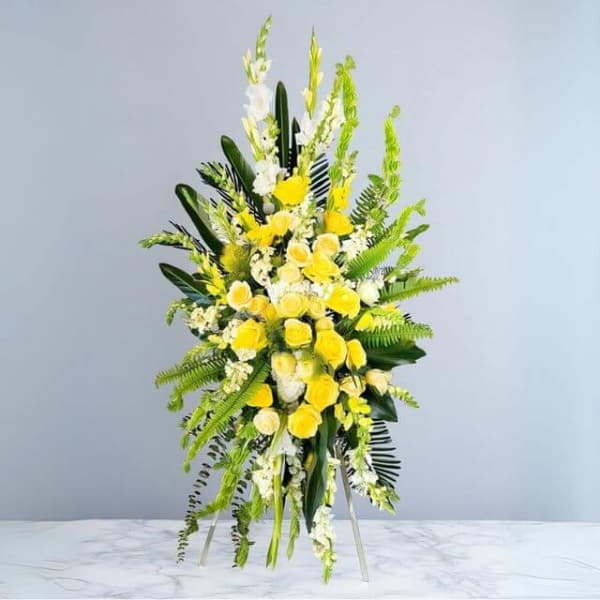 Tall standing spray of yellow and white flowers on an easel against a light background