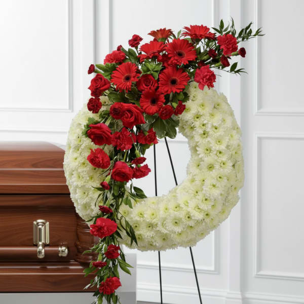 Red and white funeral wreath on a stand beside a casket