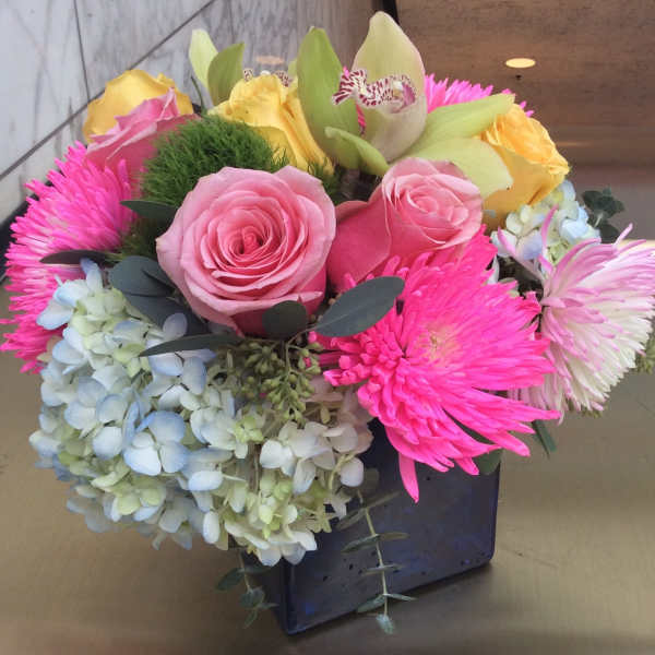 Mixed bouquet of pink roses, yellow roses, hydrangea, and bright pink mums in a black vase