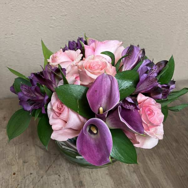 Pink roses and purple calla lilies in a glass bowl vase