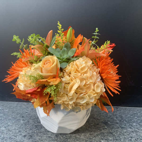 Orange and cream floral arrangement in a white vase