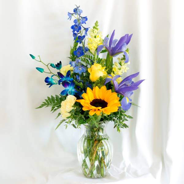 Colorful bouquet with sunflowers, irises, and blue flowers in a glass vase