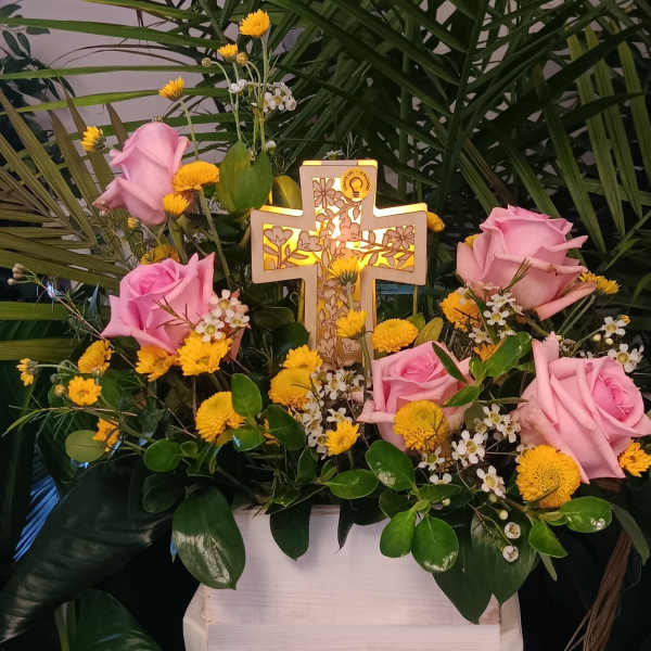 Pink roses and yellow flowers arranged around a lit decorative cross