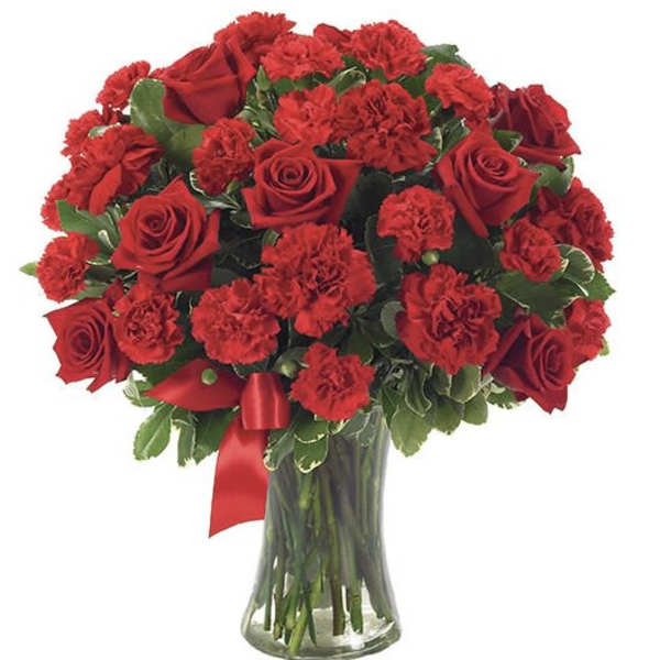 Arrangement of red roses and red carnations in a clear glass vase with a red ribbon.
