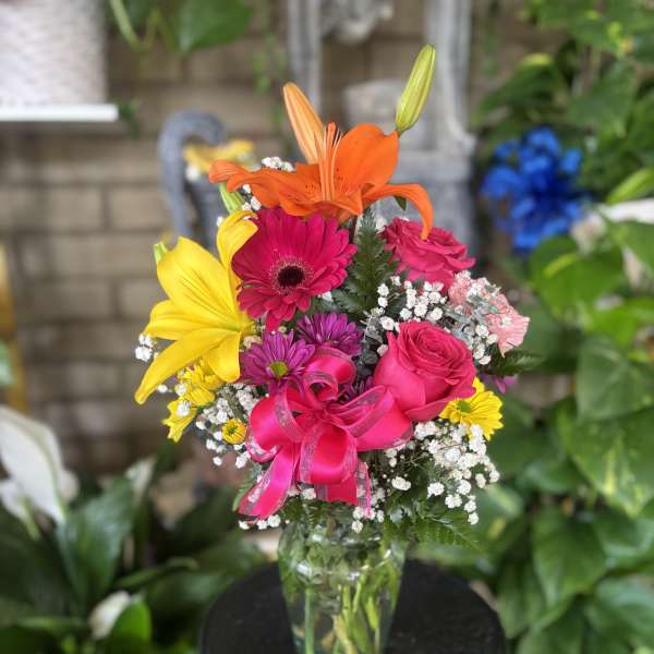 Bright mixed bouquet with lilies, roses, and a pink ribbon in a glass vase