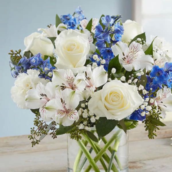 White roses and blue flowers arranged in a clear glass vase