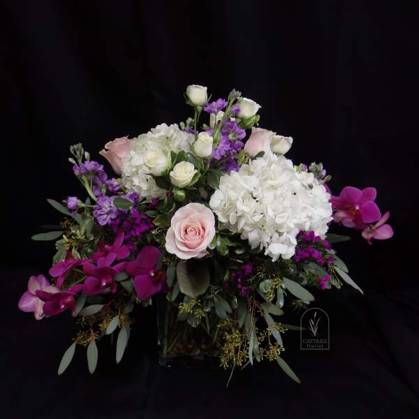 Pink and white floral arrangement with orchids and roses in a glass vase