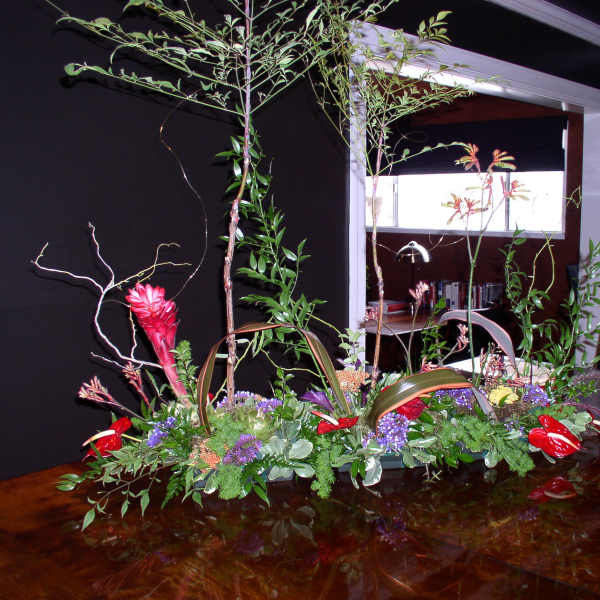 Large tropical floral centerpiece with red blooms and tall branches on a table