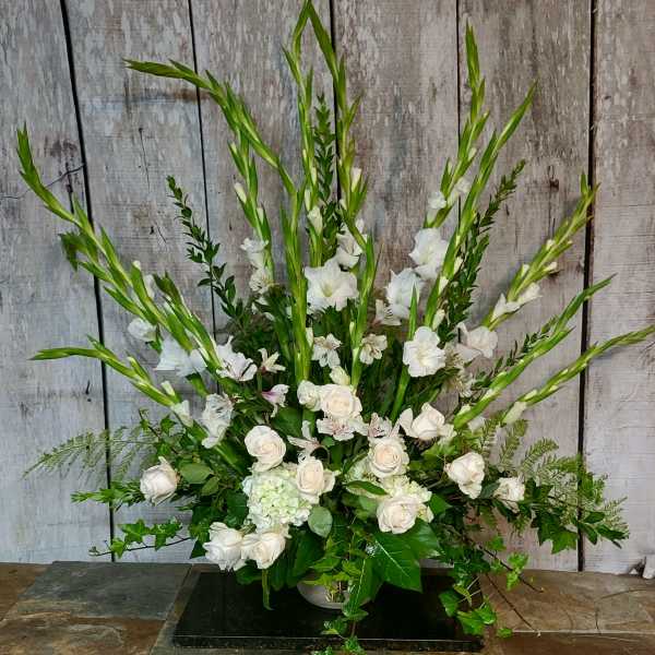 White floral arrangement with tall green spikes and roses in a low container