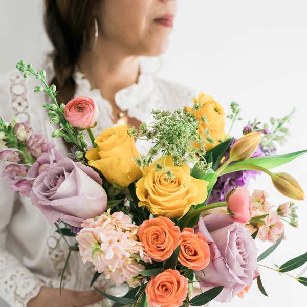 Woman holding a colorful bouquet of roses and tulips in a glass vase