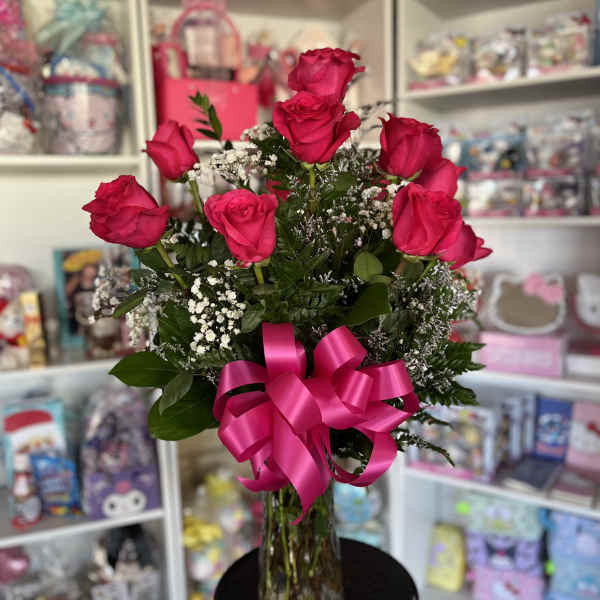 Tall arrangement of hot pink roses with white filler flowers in a clear vase with a large pink bow.