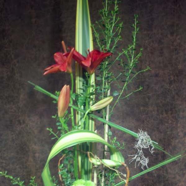 Tall floral arrangement with red lilies and succulents in a gray vase