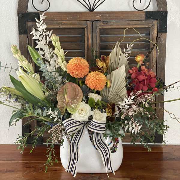 Colorful floral arrangement in a white vase with a striped ribbon