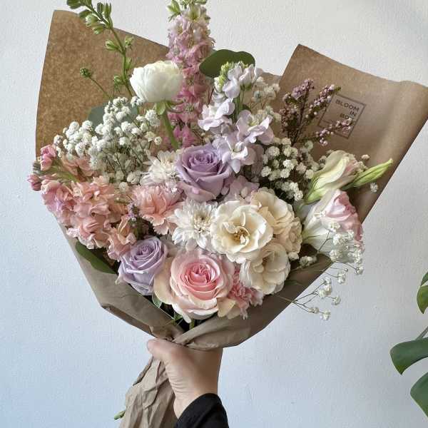 Hand-tied bouquet of pastel roses, lisianthus, and baby’s breath in brown paper