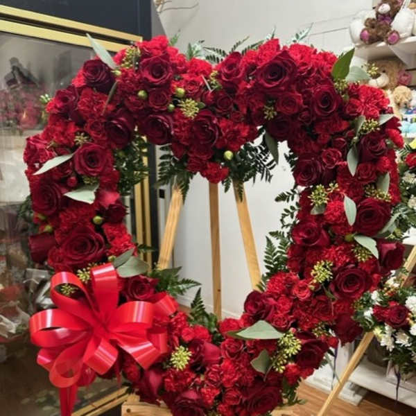 Heart-shaped red rose wreath on a wooden stand with a red ribbon