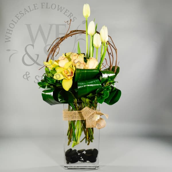 Yellow and white flowers arranged in a tall glass vase with a burlap bow