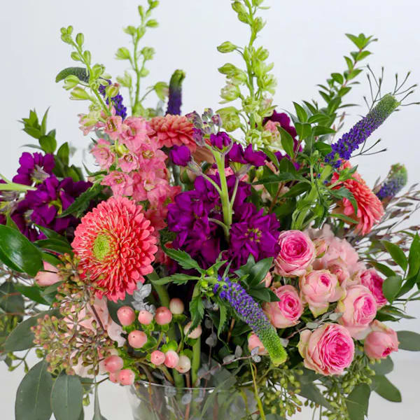 Mixed bouquet of pink and purple flowers with green spikes in a clear glass vase