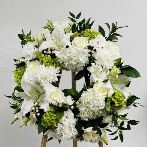 White floral wreath on a wooden easel with green accents