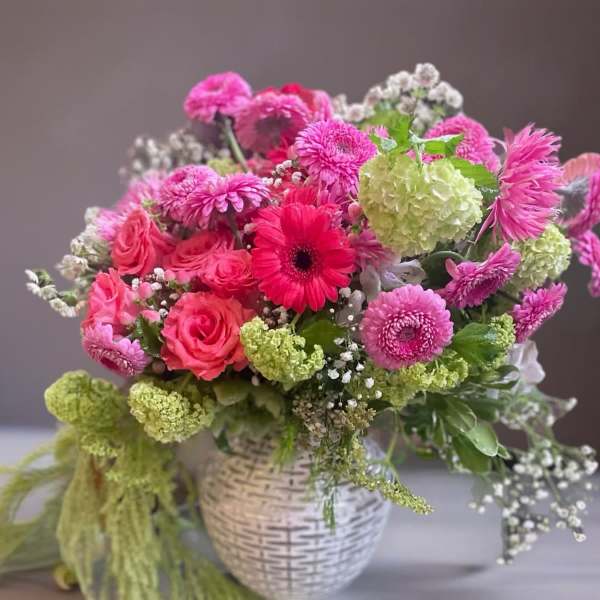 Pink and green mixed flower arrangement in a white woven vase