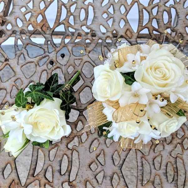 Two white floral corsages with gold ribbon and bead accents