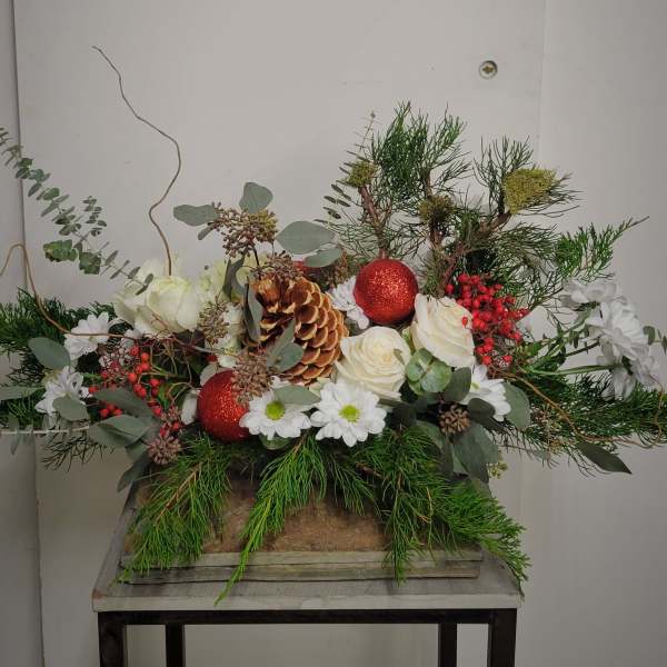 Holiday floral arrangement with white roses, daisies, pinecones, and red ornaments