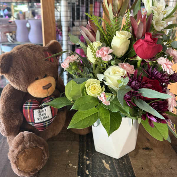 Bouquet of roses and chrysanthemums in a white vase beside a teddy bear