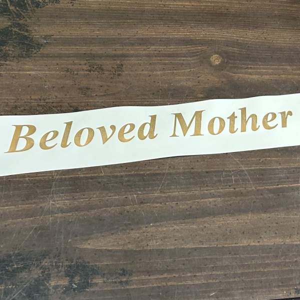 White ribbon printed with "Beloved Mother" in gold lettering