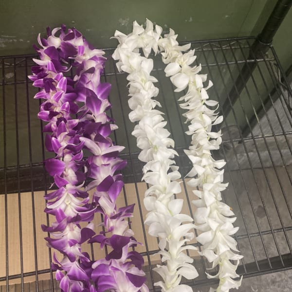 Two orchid leis, one purple and one white, laid side by side