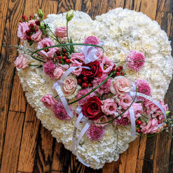 Heart-shaped white floral tribute with pink and red flowers and white name ribbons