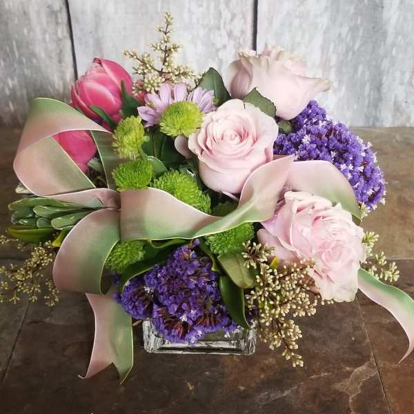Pink roses and purple flowers arranged in a glass vase with ribbon
