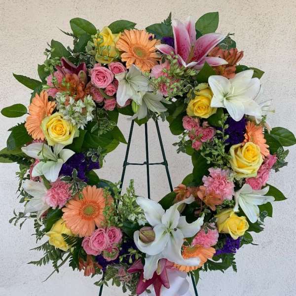 Colorful standing wreath of lilies, roses, gerbera daisies, and carnations on a metal easel