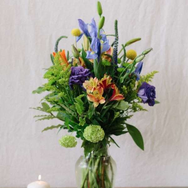 Tall mixed bouquet in a clear glass vase beside a lit candle