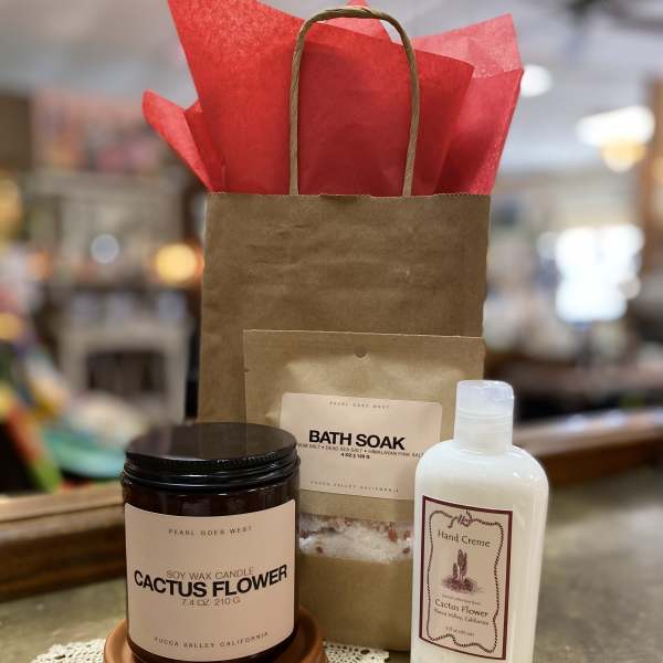 Gift set with cactus flower candle, bath soak, and hand cream beside a kraft gift bag with red tissue paper.