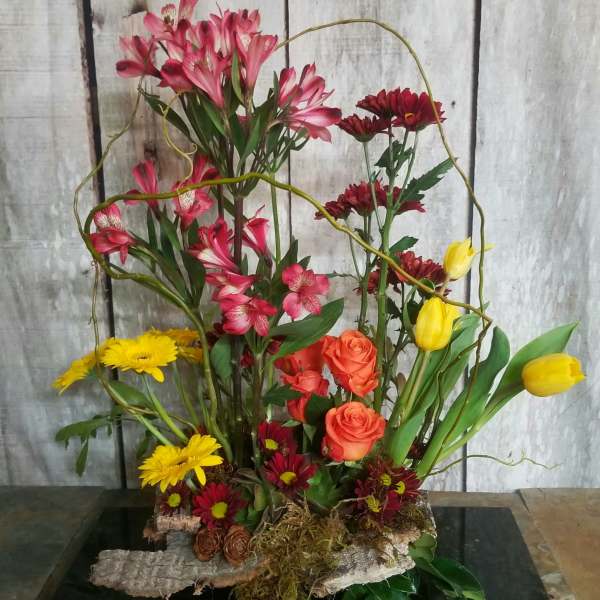 Mixed floral arrangement with pink, yellow, orange, and red blooms in a low base