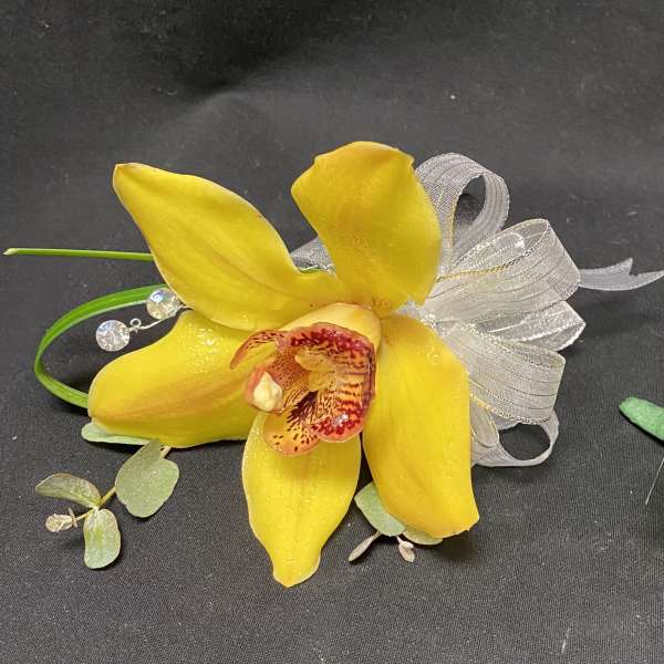Two yellow orchid corsages with ribbon and greenery on a dark background