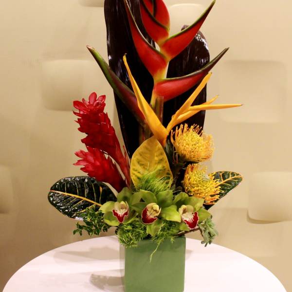 Tropical flower arrangement in a green square vase with red and yellow blooms