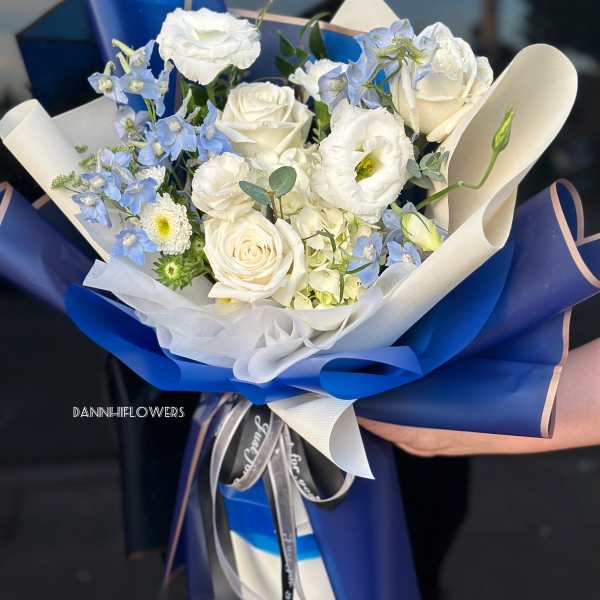 Bouquet of white roses and pale blue flowers wrapped in blue paper