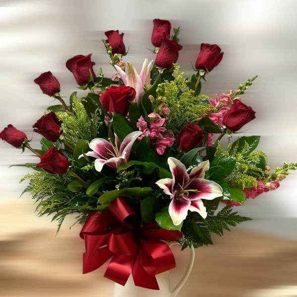 Tall arrangement of red roses and pink lilies in a white pitcher with a large red bow
